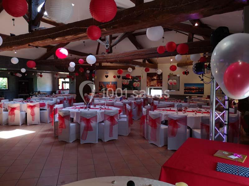 Salle de réception décorée avec des tables dressées, des chaises ornées de nœuds rouges et des lanternes suspendues.