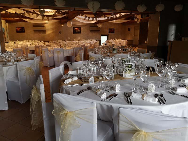 Salle de réception décorée pour un mariage, avec tables rondes dressées, nappes blanches et décorations élégantes.