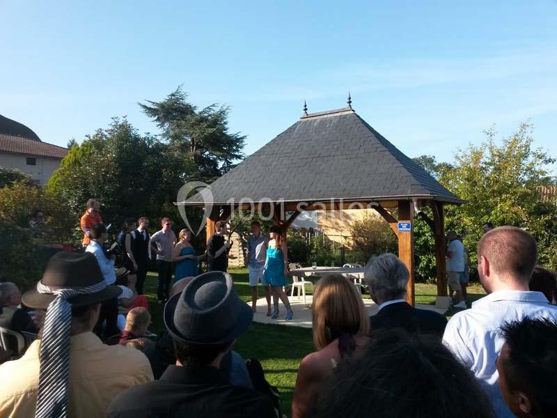 Un groupe de personnes rassemblées autour d'une pergola en bois dans un jardin par une journée ensoleillée.