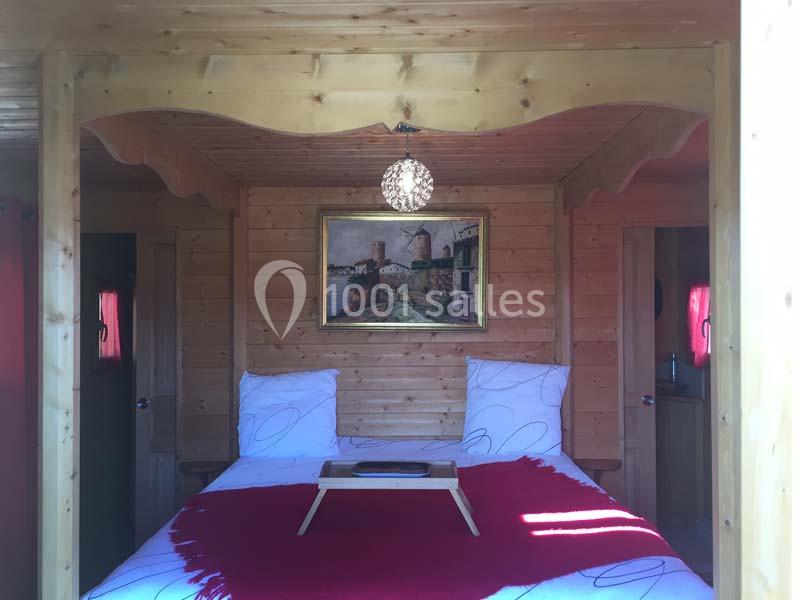 Lit double avec couverture rouge dans une chambre en bois, éclairée par une lampe suspendue et décorée d'un tableau.