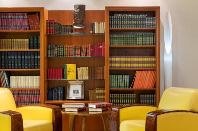 Bibliothèque avec étagères remplies de livres colorés, deux fauteuils jaunes et une table basse avec des livres ouverts.