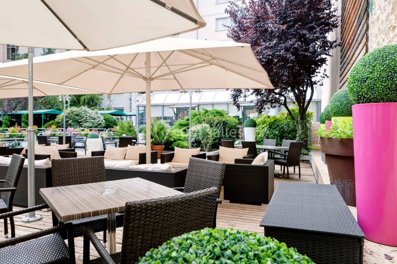 Terrasse extérieure avec tables en rotin, chaises, parasols blancs et végétation environnante.