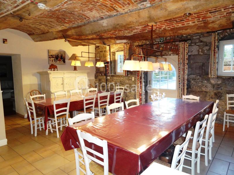 Salle à manger rustique avec plafond voûté en briques, grandes tables recouvertes de nappes rouges et chaises blanches.