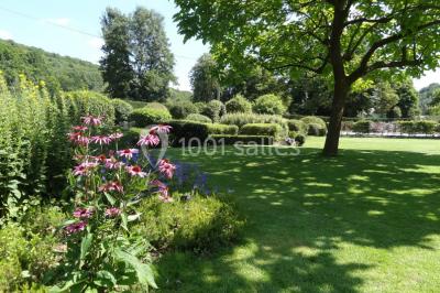 Chambre lumineuse avec deux lits simples, armoire ancienne, murs en bois et fenêtres donnant sur un jardin.