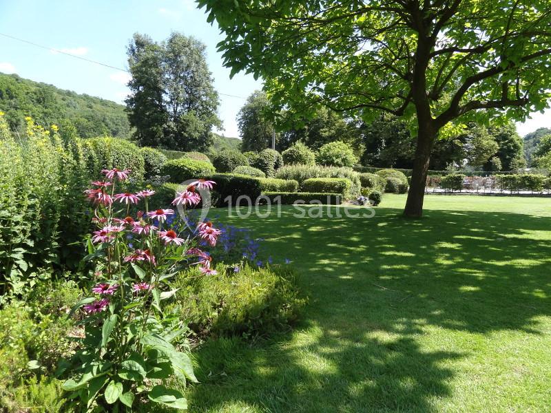 Jardin verdoyant avec pelouse, massifs de fleurs colorées et arbres sous un ciel dégagé.