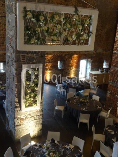 Salle de réception en briques avec tables dressées et décorations florales suspendues.