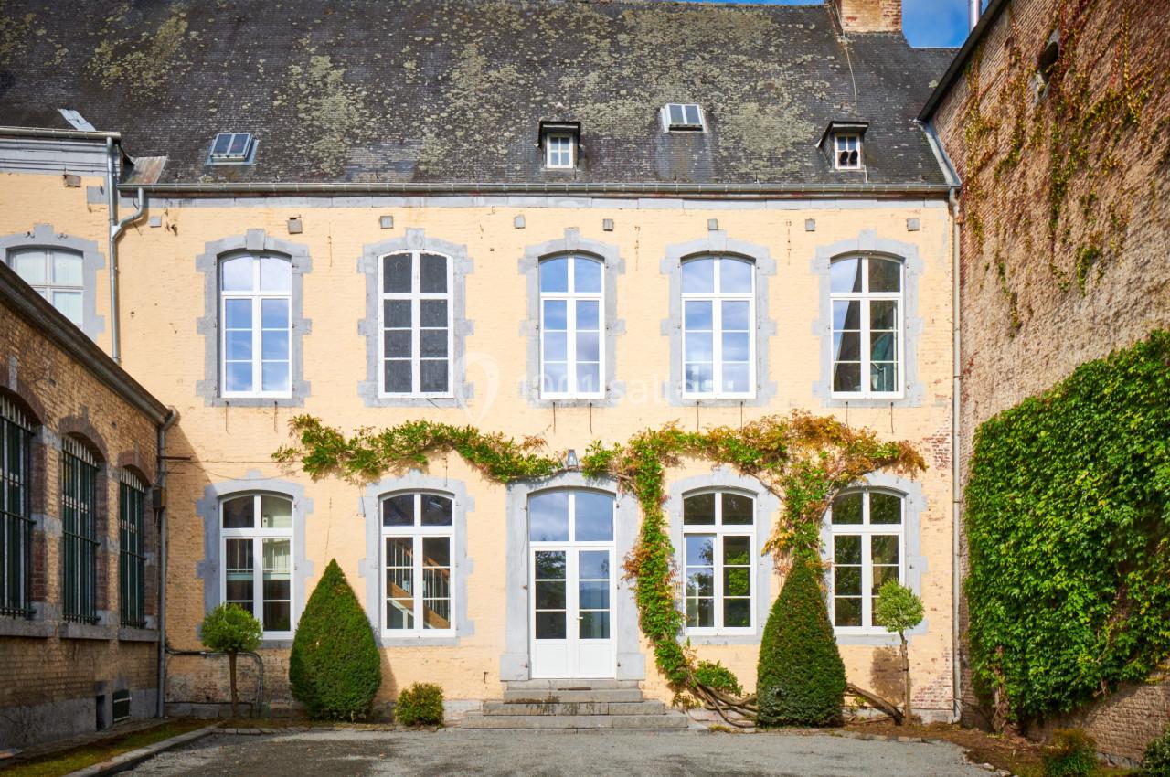 Façade d'un bâtiment ancien en briques jaunes avec des fenêtres blanches et des plantes grimpantes.