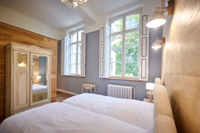 Chambre lumineuse avec deux lits simples, armoire ancienne, murs en bois et fenêtres donnant sur un jardin.