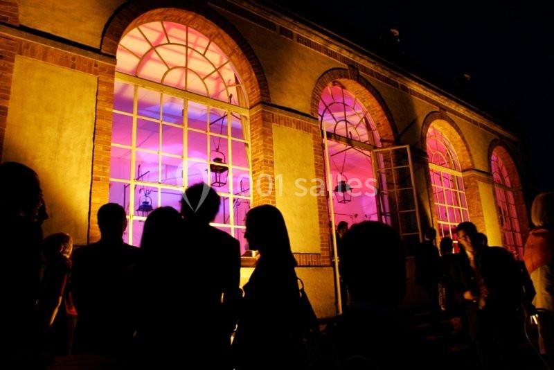 Silhouettes de personnes devant un bâtiment éclairé de lumières roses à travers de grandes fenêtres en arc.