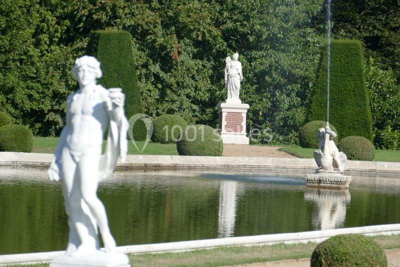 Statues en marbre autour d'un bassin dans un jardin avec des haies taillées et une fontaine.