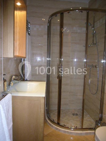 Salle de bain avec cabine de douche arrondie en verre, lavabo intégré dans un meuble en bois et carrelage beige.