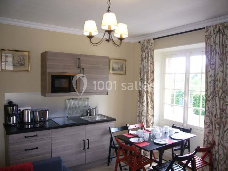 Cuisine équipée avec micro-ondes, cafetière et évier, table dressée pour quatre personnes près d'une fenêtre lumineuse.