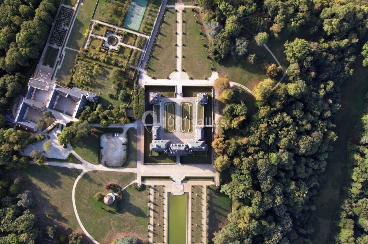 Vue aérienne d'un château entouré de jardins symétriques, d'allées et d'une forêt dense.