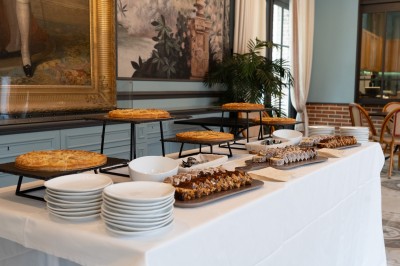 Miniature Goûter au Café d'Achille Table dressée avec des assiettes, des plats de tartes et de desserts variés, dans une salle décorée de tableaux et de…