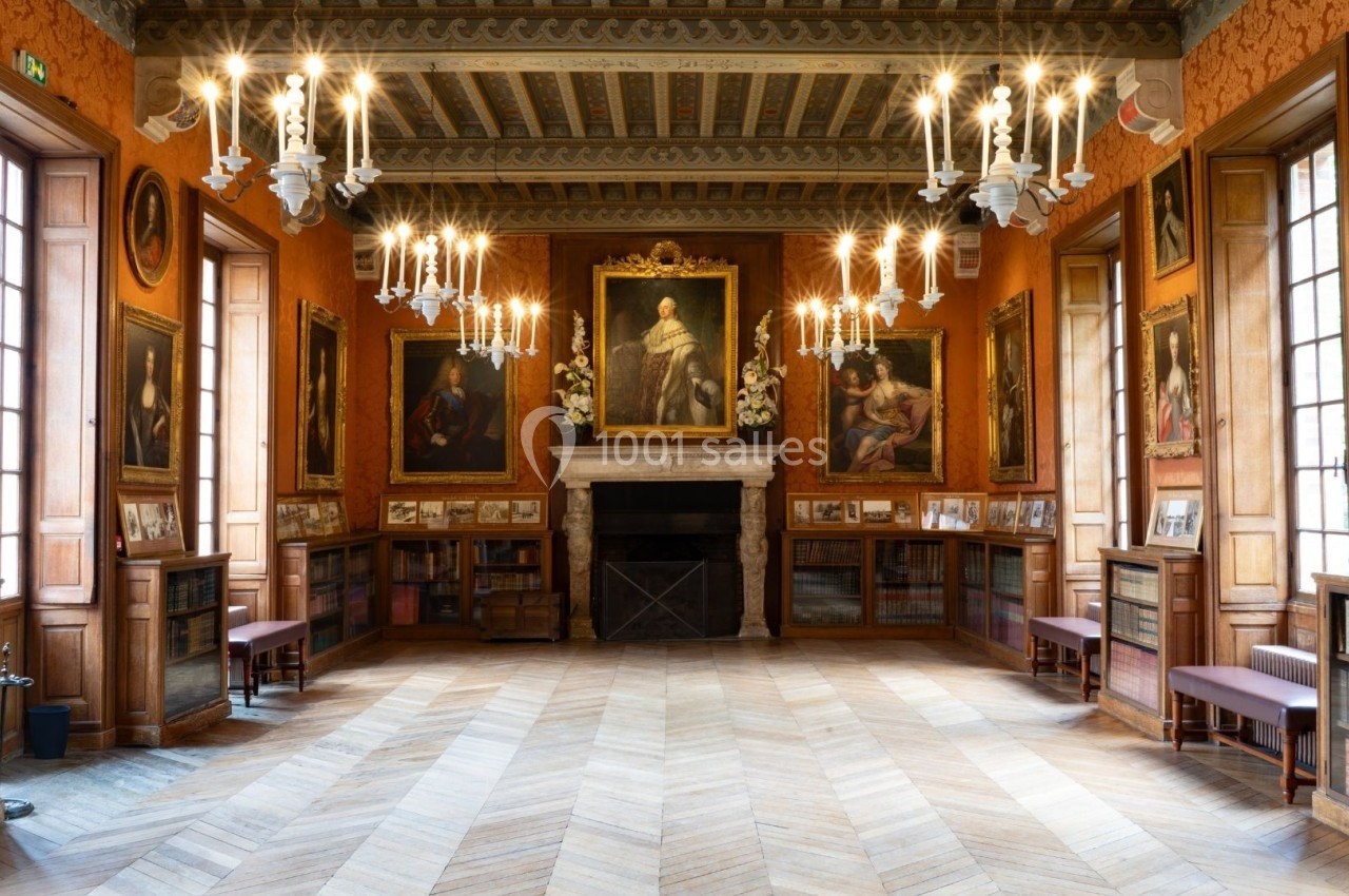 Salle ornée de portraits et de peintures, avec un plafond décoré, des chandeliers suspendus et des étagères de livres.