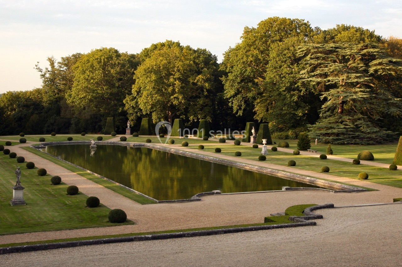 Jardin à la française avec bassin central rectangulaire, pelouses bordées d'arbres et arbustes taillés.