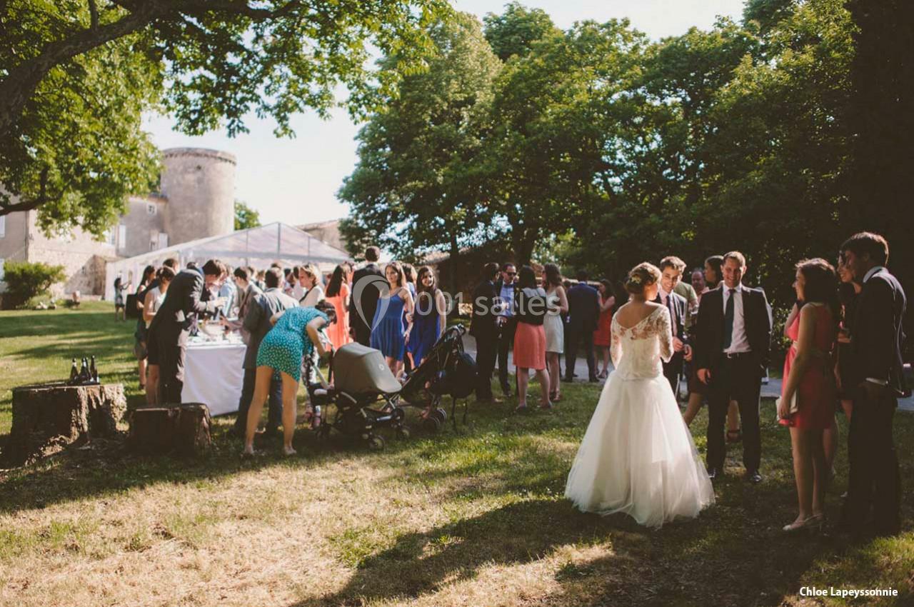 Groupe de personnes rassemblées en extérieur lors d'une réception, avec une mariée en robe blanche au premier plan.