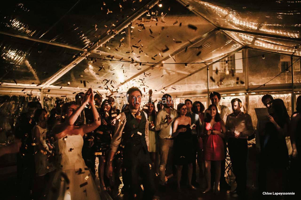 Des invités célèbrent sous une tente éclairée, entourés de confettis et d'une ambiance festive.
