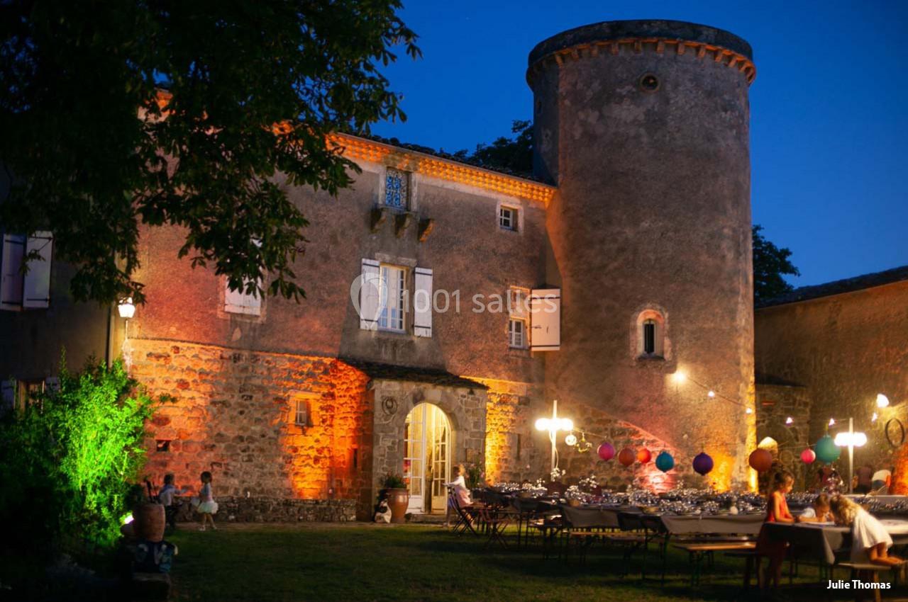 Façade d'un château ancien éclairé, avec une table dressée et des décorations colorées dans le jardin au crépuscule.