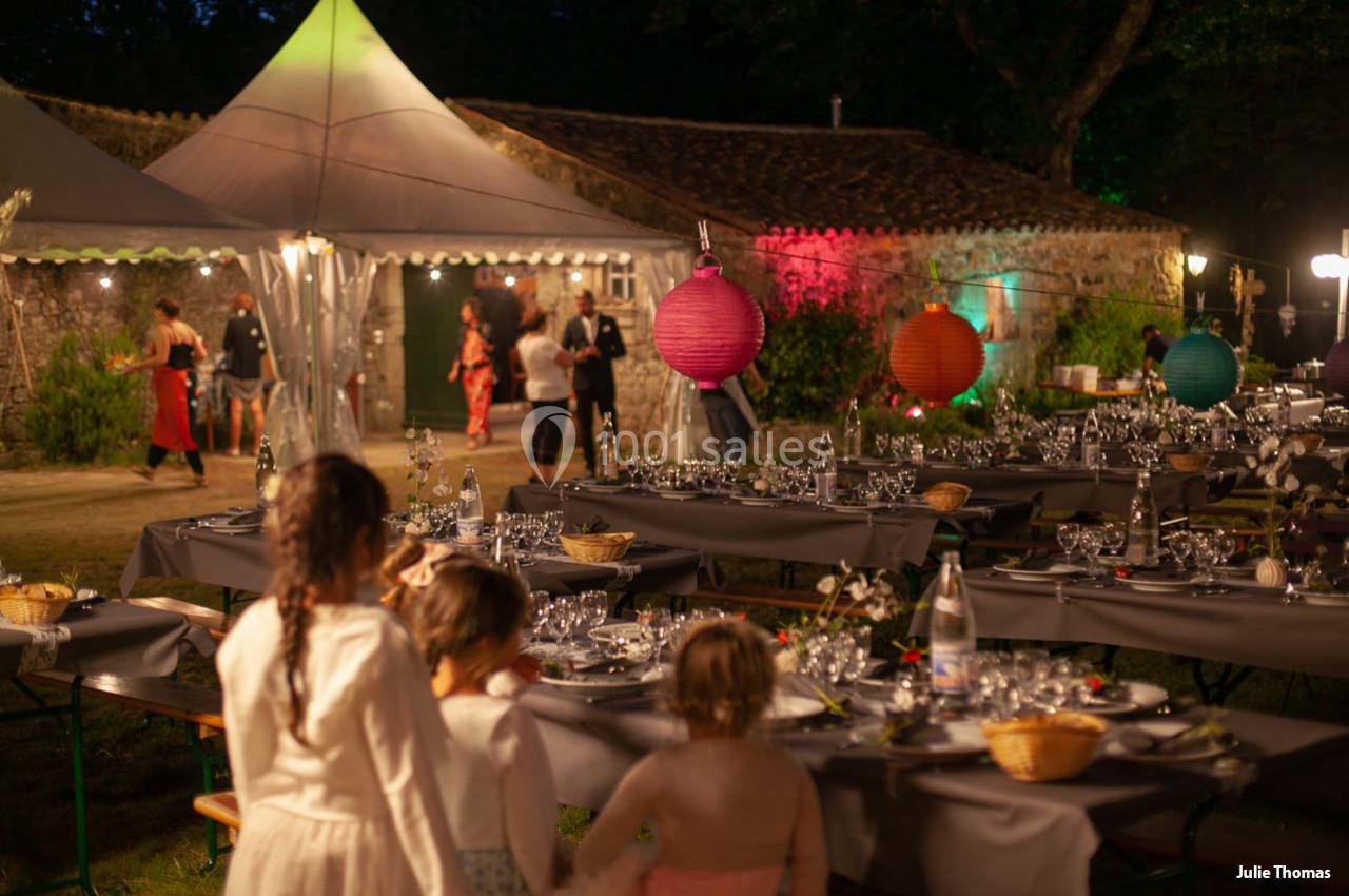 Des enfants observent des tables dressées pour un dîner en plein air, avec des lanternes colorées et des invités en arrière…