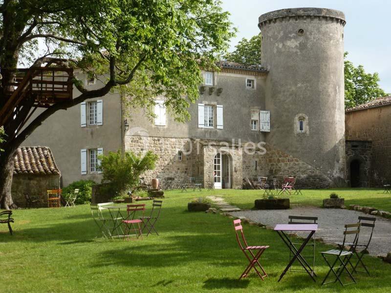Château en pierre avec tour ronde, entouré d'un jardin verdoyant et de tables de jardin colorées.