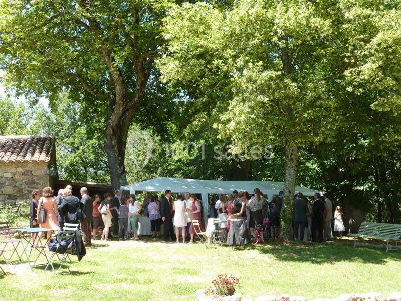 Groupe de personnes rassemblées en extérieur sous des arbres près d'une tente blanche, par une journée ensoleillée.