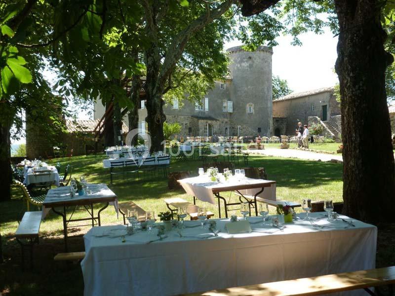 Tables dressées pour un repas en plein air sous des arbres, avec un château en pierre en arrière-plan.