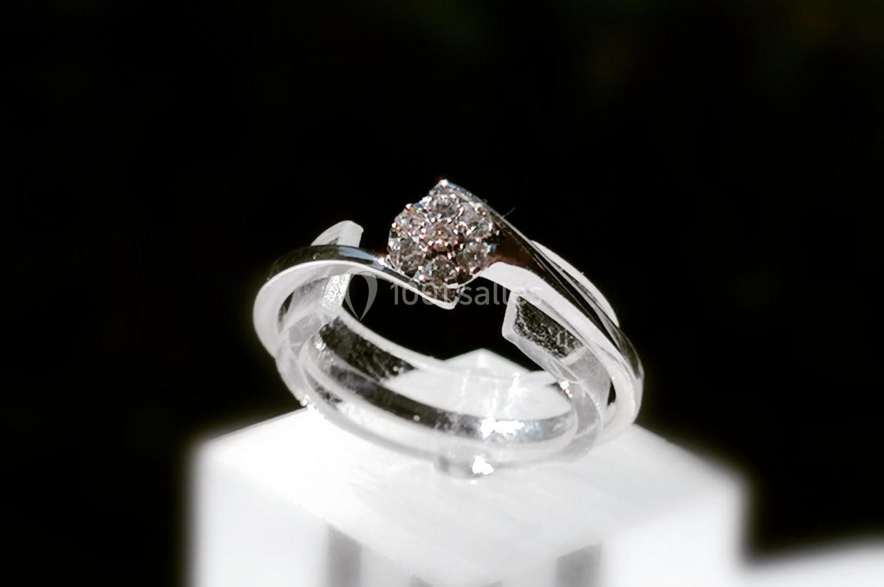 Bague en argent ornée d'un diamant central, posée sur un support blanc avec un arrière-plan sombre.