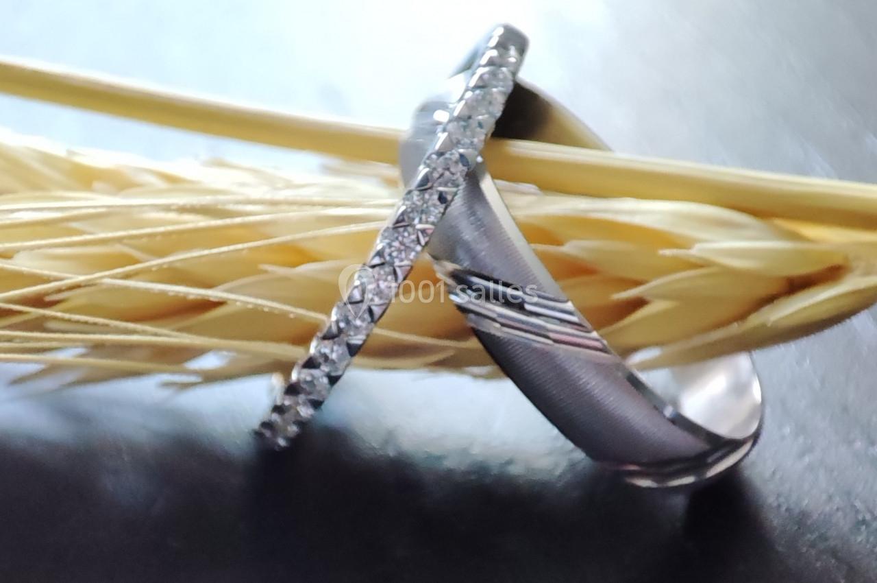 Deux alliances en métal, dont une sertie de diamants, posées sur un épi de blé sur une surface sombre.