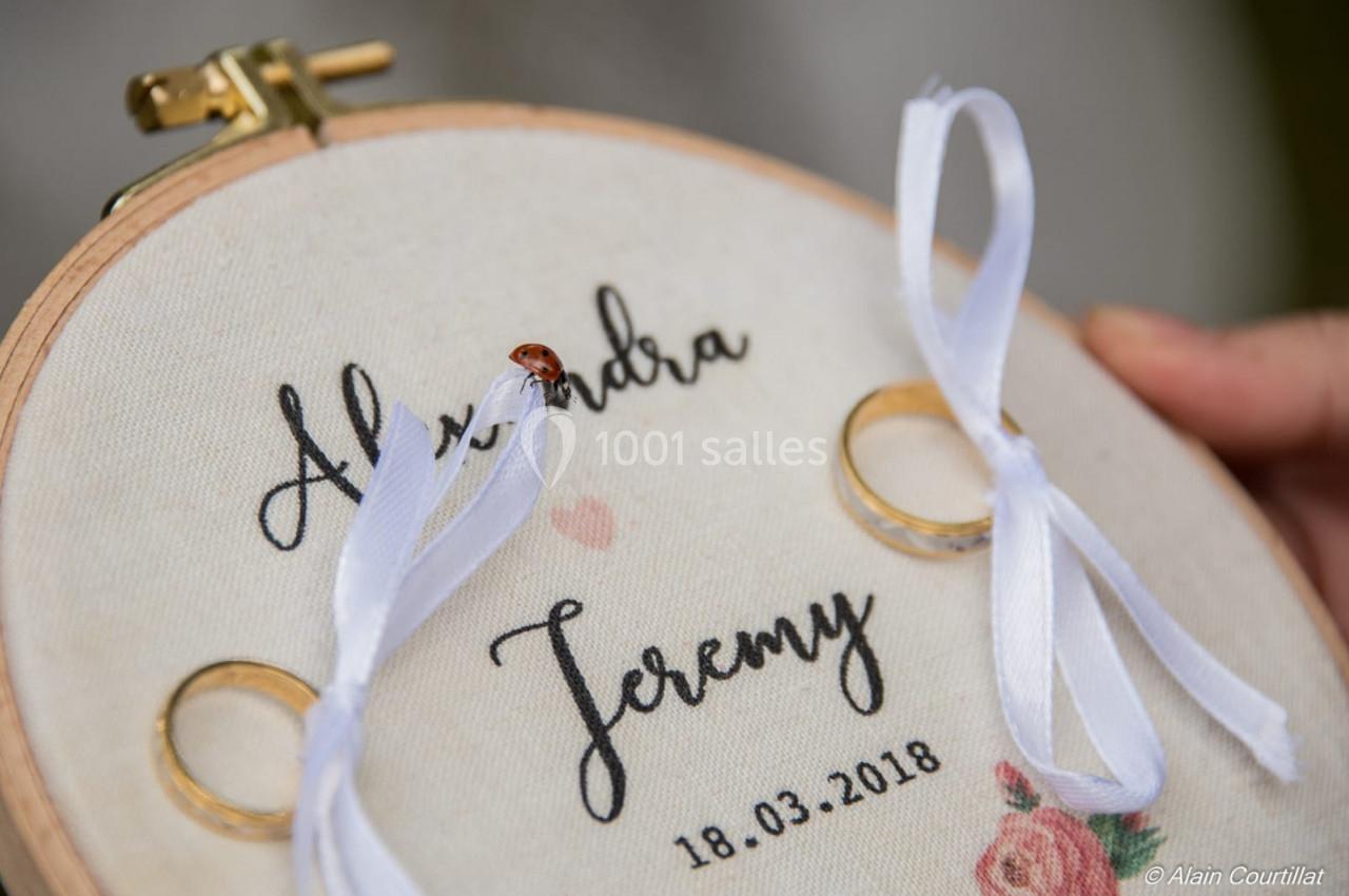 Cercle à broder décoré avec des alliances, des rubans blancs et une coccinelle posée sur le tissu brodé.