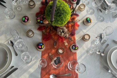 Table dressée avec une nappe blanche, chemin de table orange, décorations automnales et vaisselle élégante.