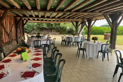 Salle de réception rustique avec poutres en bois apparentes, tables rondes dressées et chaises rouges.
