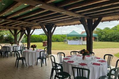 Salle de réception rustique avec poutres en bois apparentes, tables rondes dressées et chaises rouges.