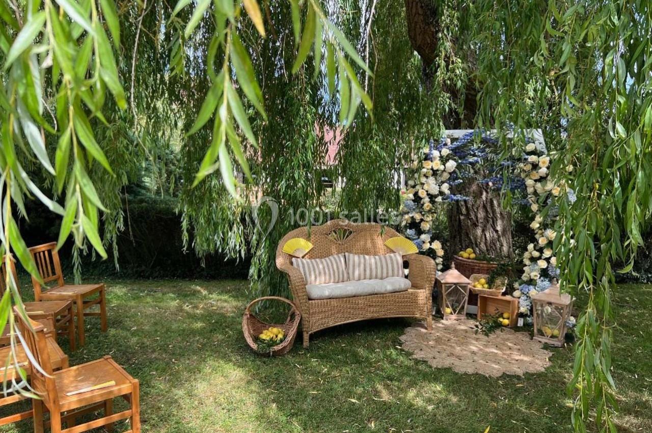 Espace extérieur décoré avec un canapé en osier, des fleurs, des chaises en bois et des branches de saule tombantes.