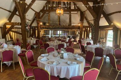 Salle de réception rustique avec poutres en bois apparentes, tables rondes dressées et chaises rouges.
