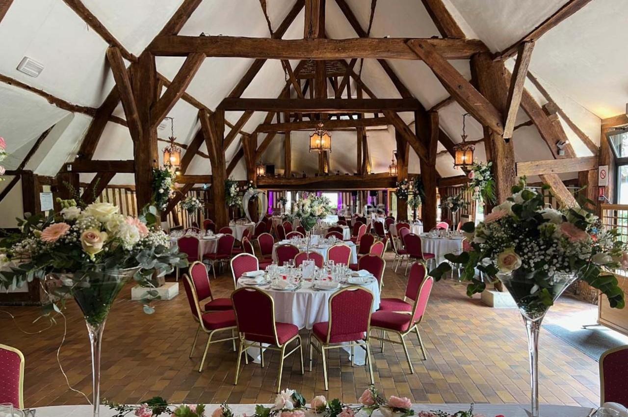 Salle de réception rustique avec poutres apparentes, tables dressées et décor floral pour un événement festif.