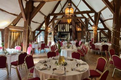 Salle de réception rustique avec poutres en bois apparentes, tables rondes dressées et chaises rouges.