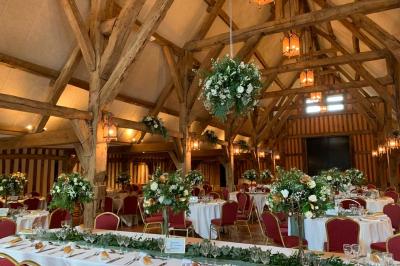 Salle de réception rustique avec poutres en bois apparentes, tables rondes dressées et chaises rouges.