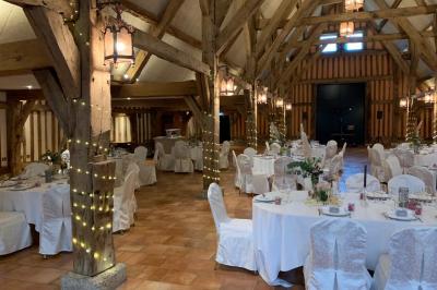 Salle de réception rustique avec poutres en bois apparentes, tables rondes dressées et chaises rouges.