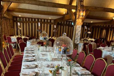 Salle de réception rustique avec poutres en bois apparentes, tables rondes dressées et chaises rouges.