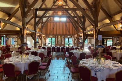 Salle de réception rustique avec poutres en bois apparentes, tables rondes dressées et chaises rouges.