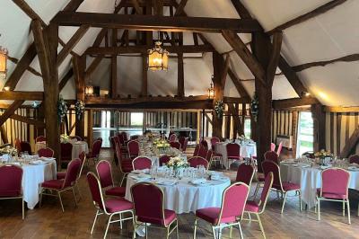 Salle de réception rustique avec poutres en bois apparentes, tables rondes dressées et chaises rouges.