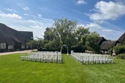 Salle de réception rustique avec poutres en bois apparentes, tables rondes dressées et chaises rouges.