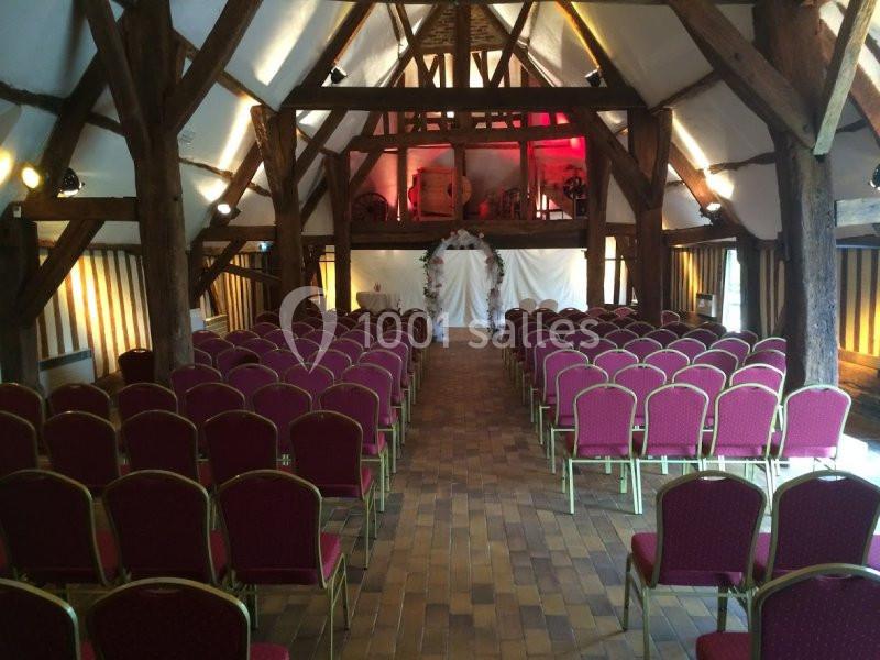 Salle avec poutres apparentes, rangées de chaises rouges alignées face à une arche décorée pour une cérémonie.