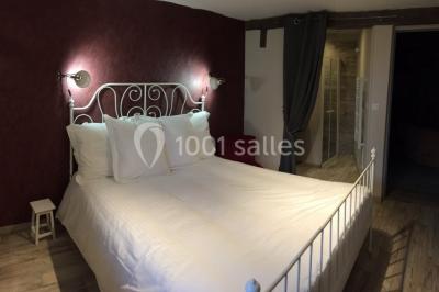 Salle de réception rustique avec poutres en bois apparentes, tables rondes dressées et chaises rouges.