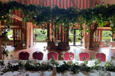 Salle de réception rustique avec poutres en bois apparentes, tables rondes dressées et chaises rouges.