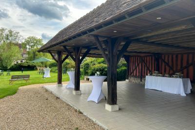 Salle de réception rustique avec poutres en bois apparentes, tables rondes dressées et chaises rouges.
