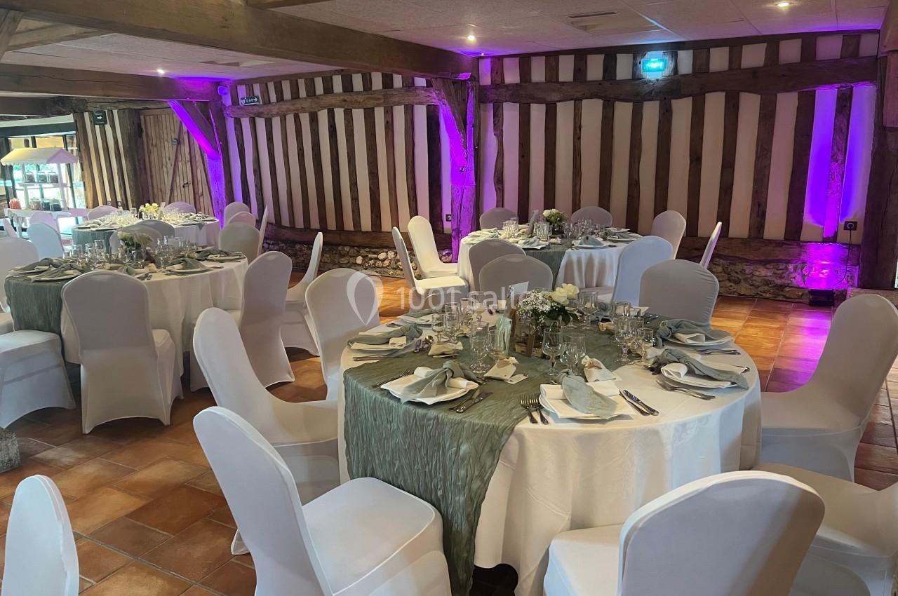 Salle de réception avec tables rondes dressées, nappes blanches et décorations florales, éclairage violet en arrière-plan.