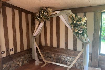 Salle de réception rustique avec poutres en bois apparentes, tables rondes dressées et chaises rouges.