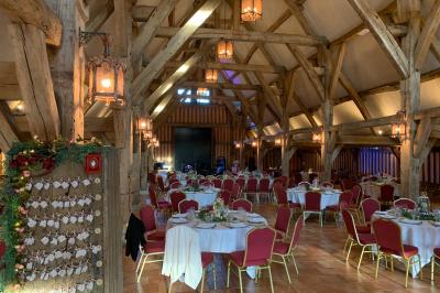 Salle de réception rustique avec poutres en bois apparentes, tables rondes dressées et chaises rouges.